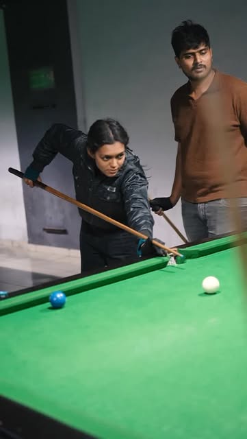 A player lining up a shot on the pool table while another looks on