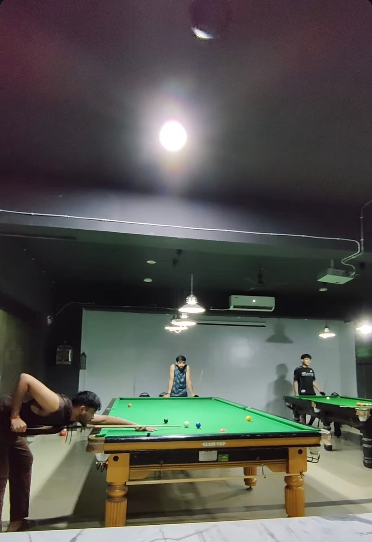 A player bent low over the snooker table lining up a shot while two others look on