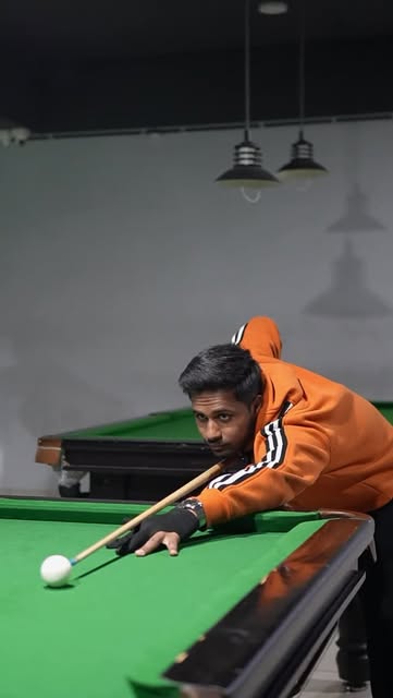 A player in an orange hoodie taking a shot on the snooker table